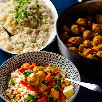 single serving of Thai red curry meatballs in a bowl with jasmine rice and pot of meatballs in the back