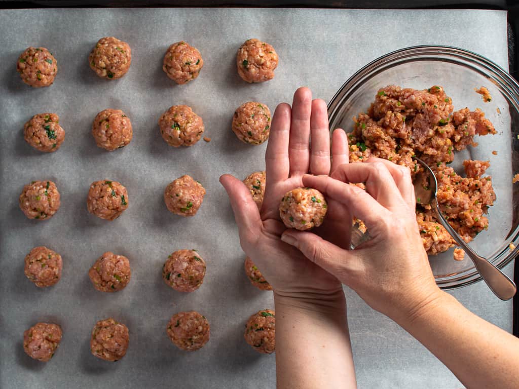 meatball shaping with one in hand and some on a baking sheet