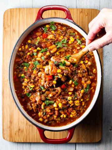 One pot of vegetarian 3 bean chili with wooden spoon being held to show ingredients