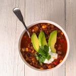 single bowl of vegetarian 3 bean chili garnished with sliced avocado, cilantro and sour cream