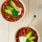 2 bowls vegetarian 3 bean chili garnished with avocado, sour cream and cilantro