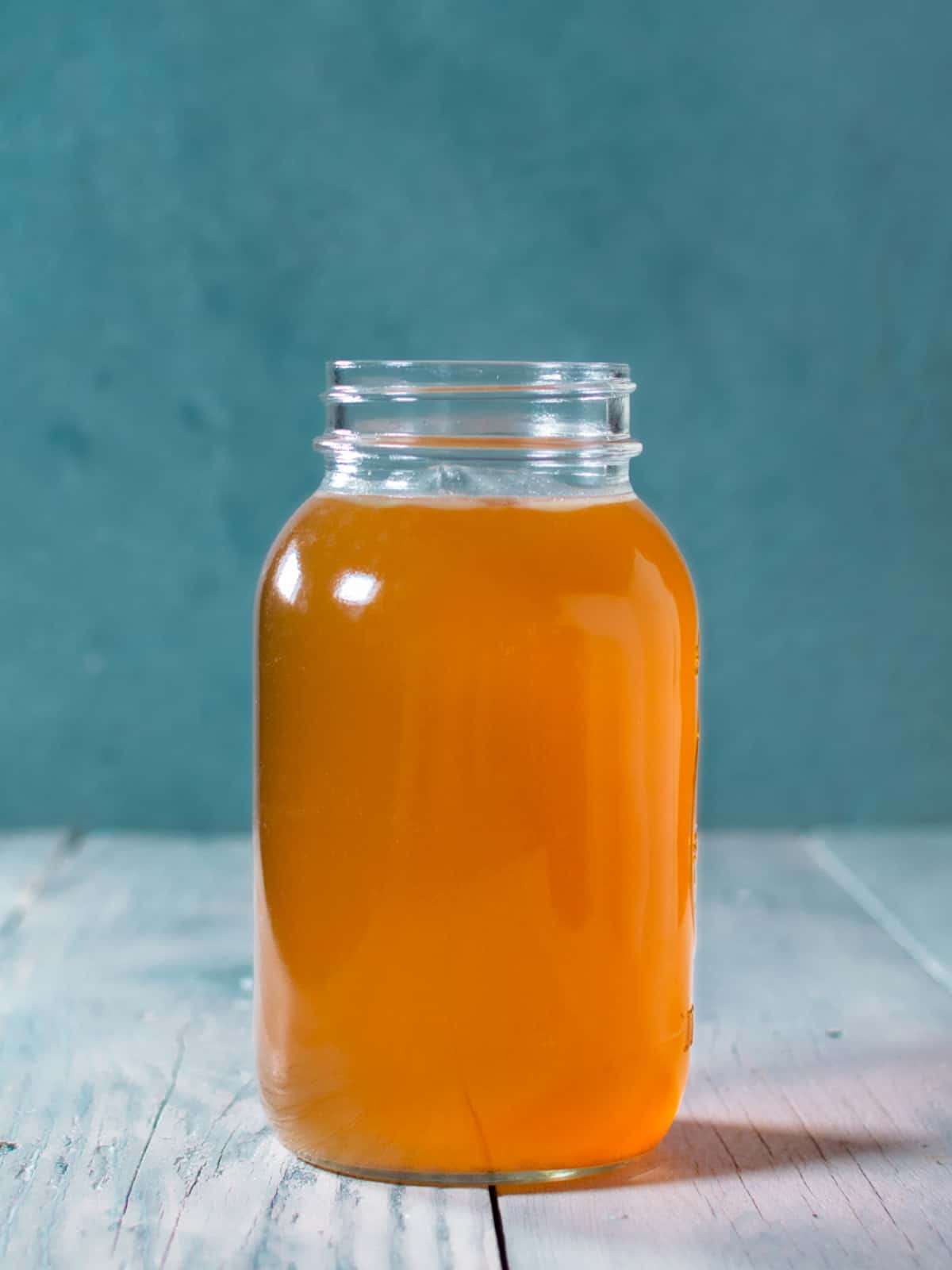 One liter mason jar of chicken stock with blue background.