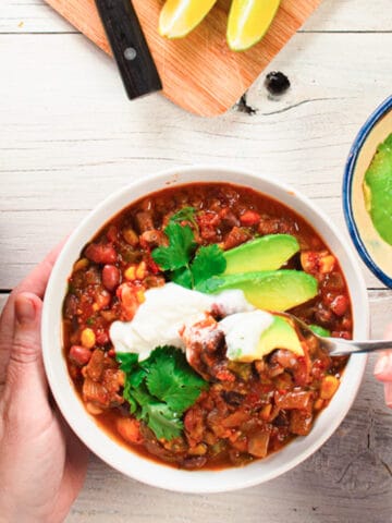 One serving of chili garnished with avocado and sour cream. A spoonful is being lifted out of the dish.