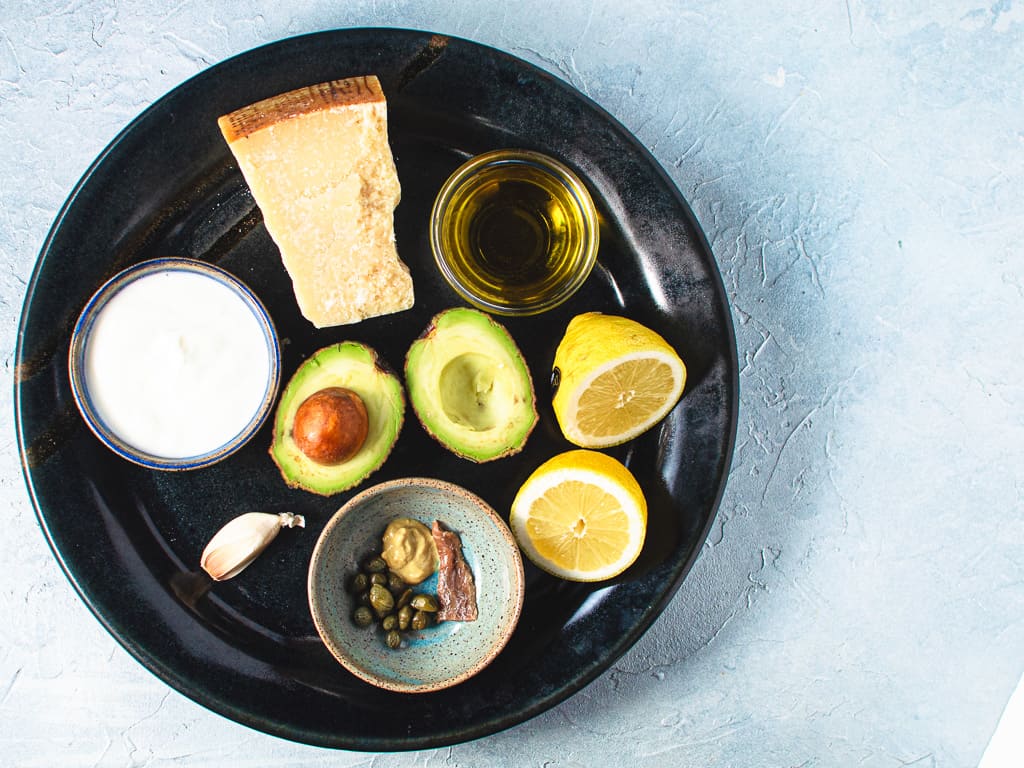all ingredients for kale and avocado Caesar salad on black ceramic platter