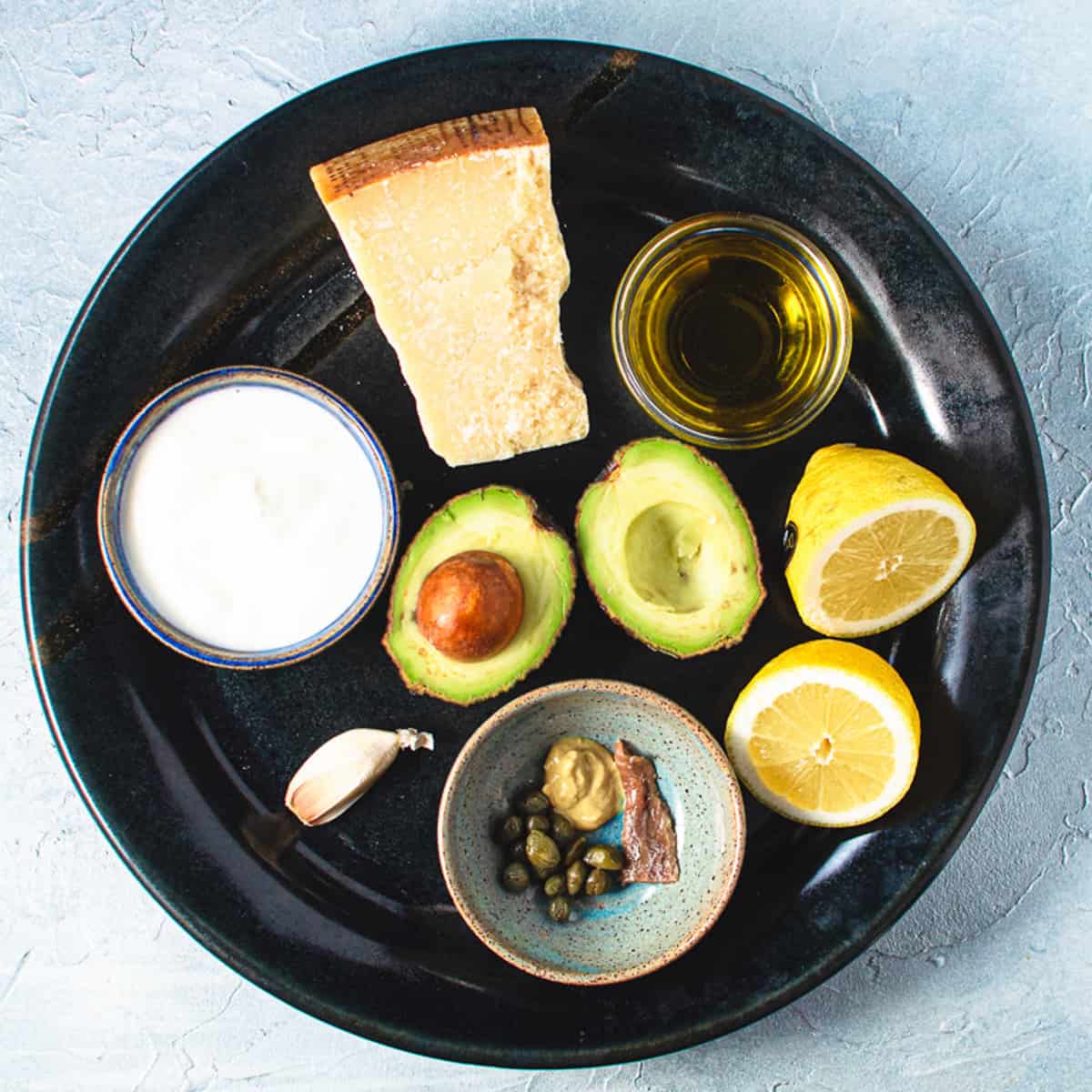 all ingredients for kale and avocado Caesar salad on black ceramic platter.