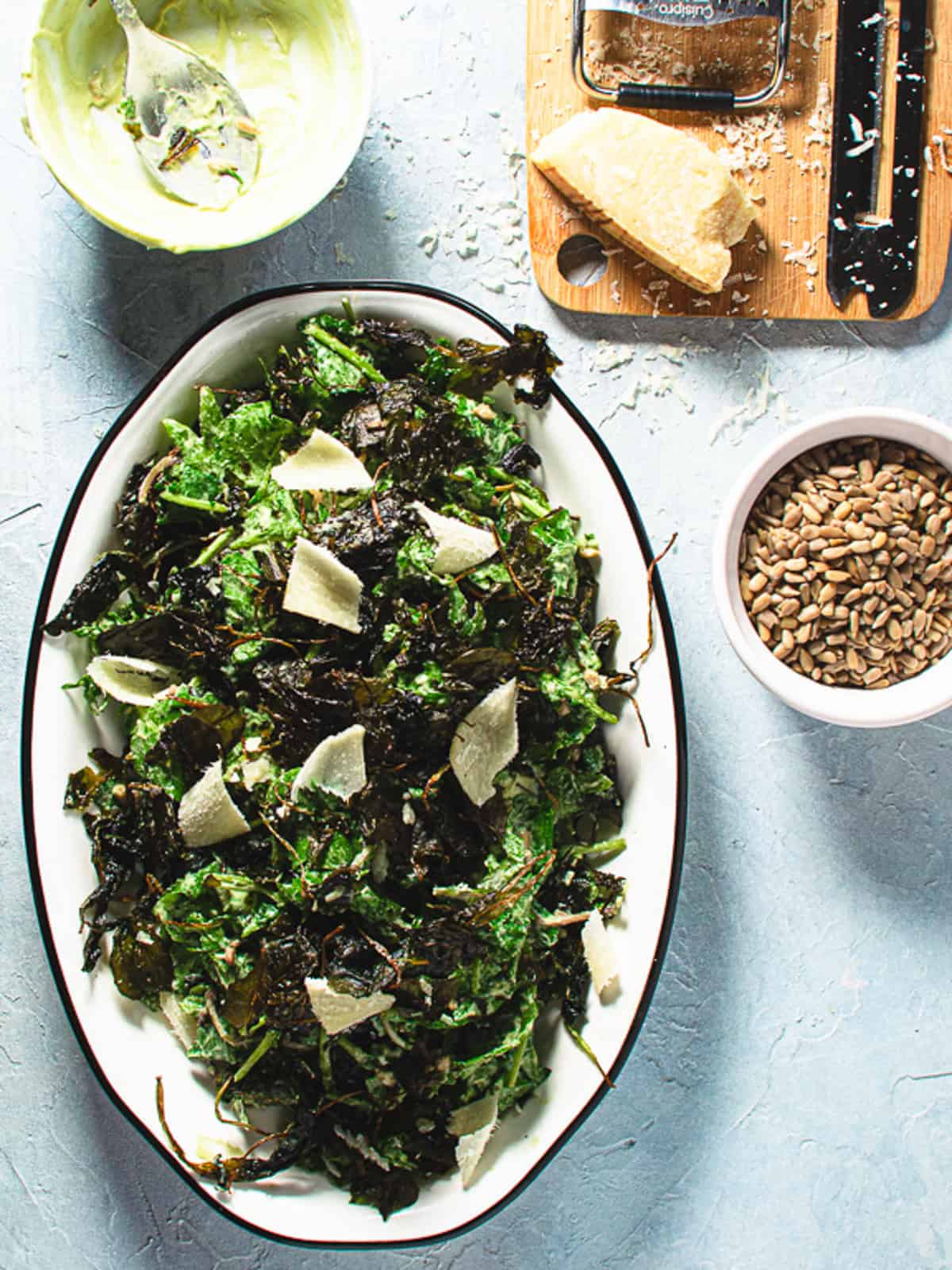 kale caesar on an oval plate with salad dressing, parmesan cheese and sunflower seeds on the side. 