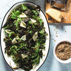 kale salad garnished with parmesan cheese with a dish of sunflower seeds on the side.