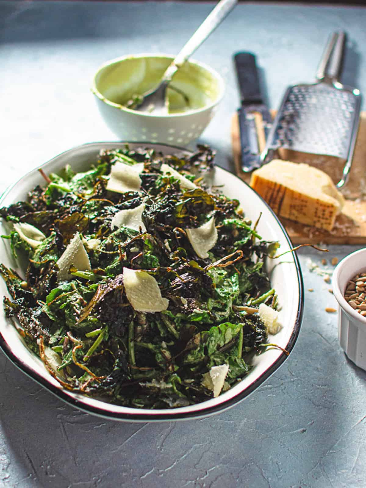 kale caesar salad on white oval platter with parmesan cheese, sunflower seeds and empty dressing bowl on the side.