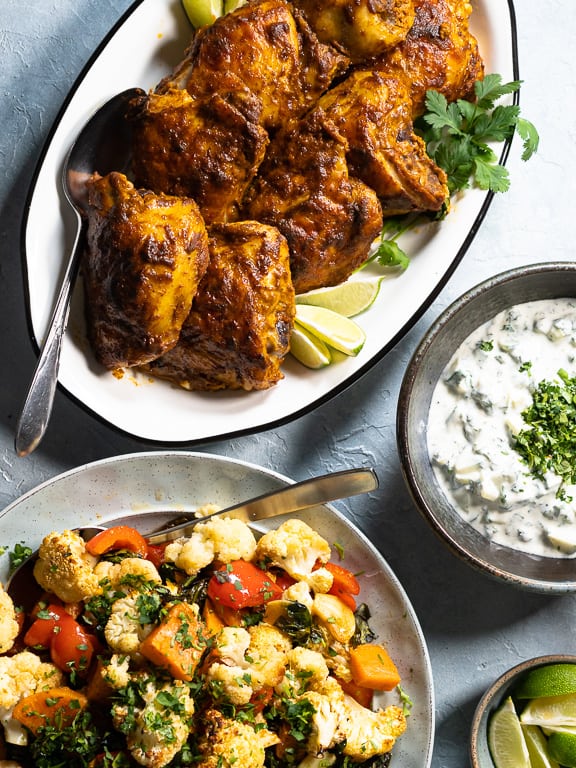 Curried chicken, vegetables and Cucumber Raita in seperate dishes on blue background
