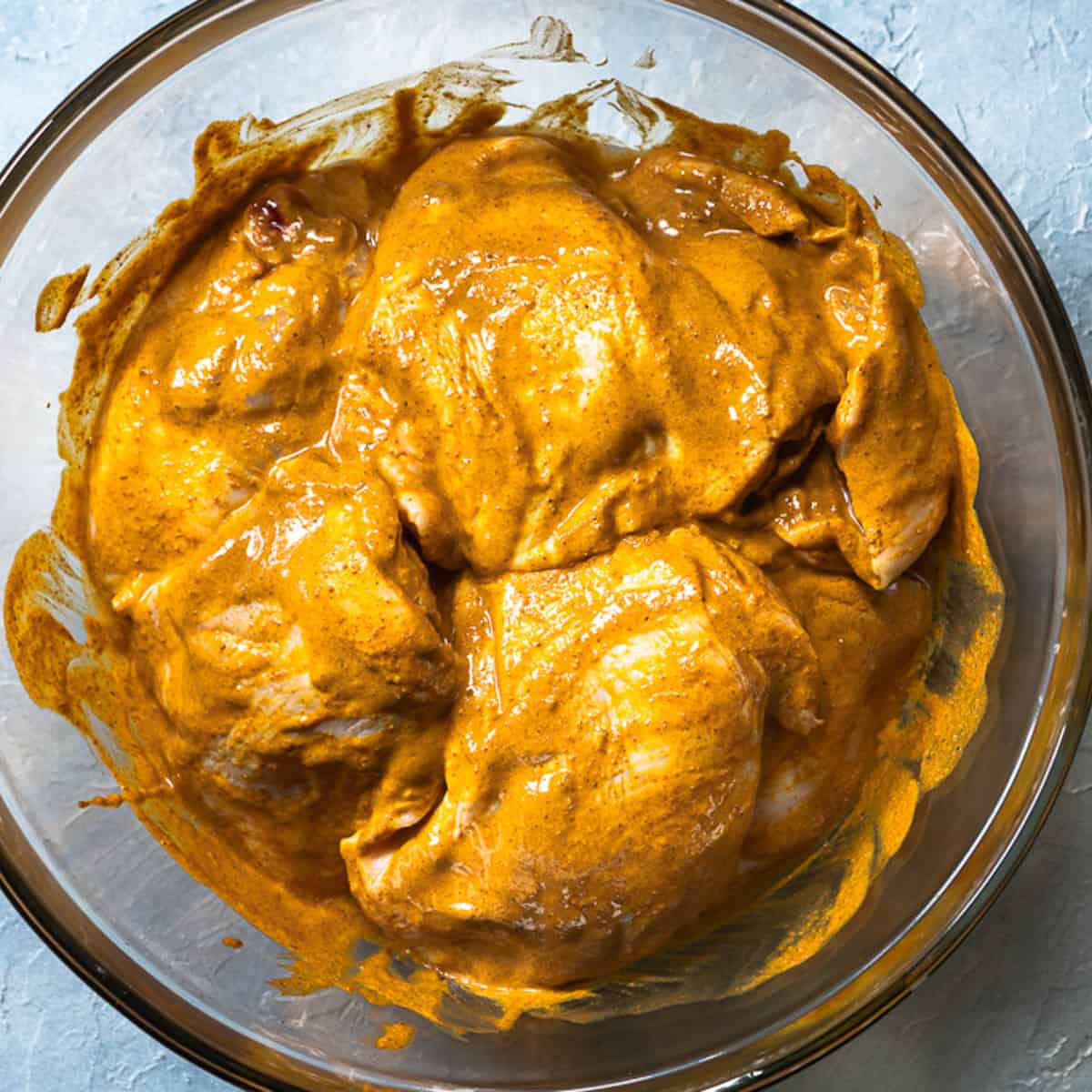 chicken thighs marinating in a clear glass bowl. 