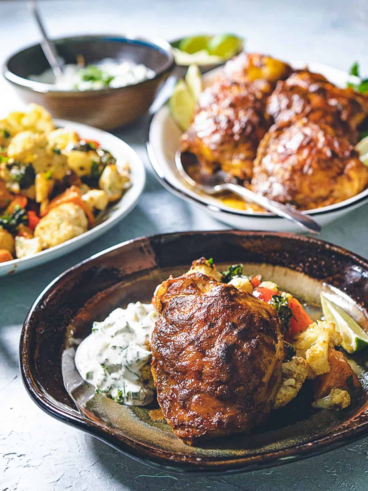 one serving of curried chicken on a plate with vegetables and cucumber raita. 