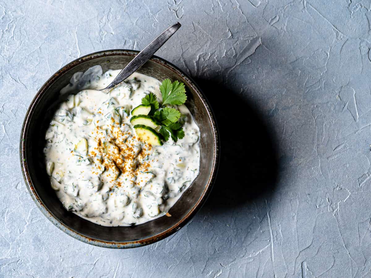 one recipe of raita in a black ceramic bowl garnished with fresh cucumber slices, cilantro and paprika. 