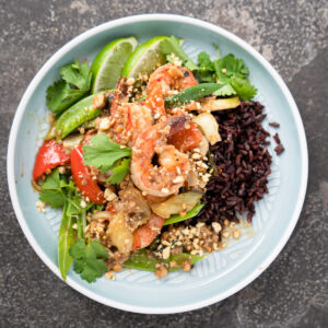 An individual portion of shrimp stir fry served over black rice with fresh lime wedges on the side.