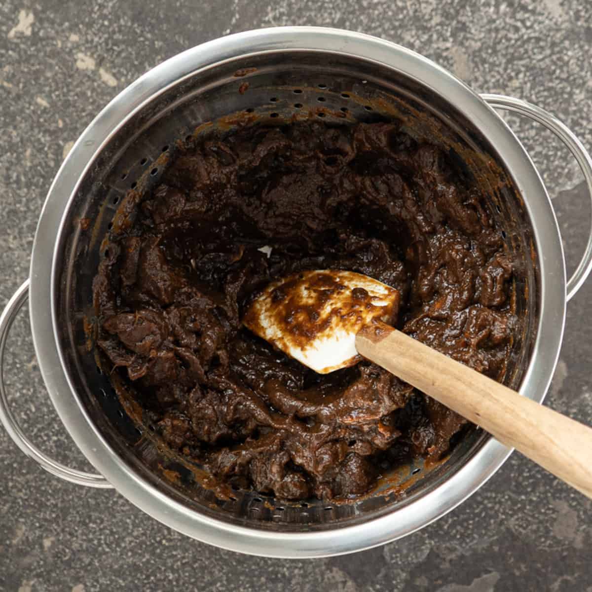 pushing soaked tamarind pulp through a colander using a rubber spatula.