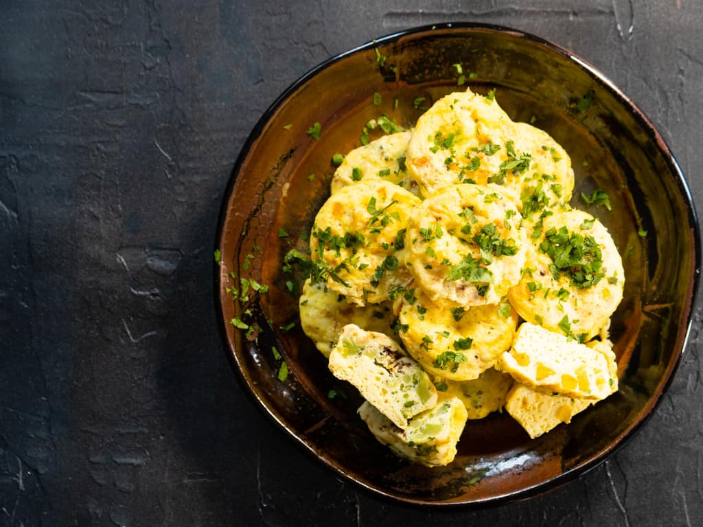 Pile of egg bites on brown pottery plate on black background