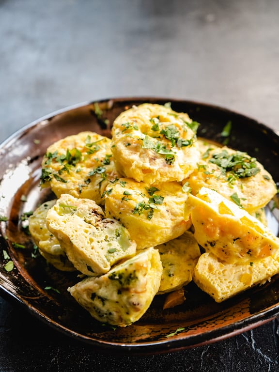 Egg bites in a pile on a pottery dish. Two are cut in half to show inside