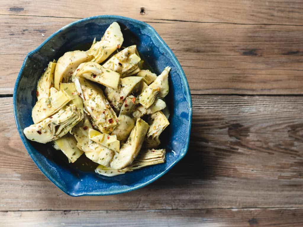marinated artichoke hearts in a blue ceramic dish on a wooden background.