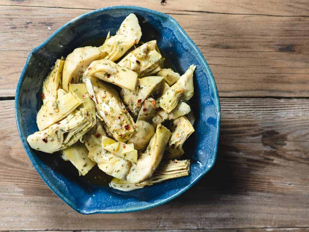 marinated artichoke hearts in blue ceramic bowl on wood background