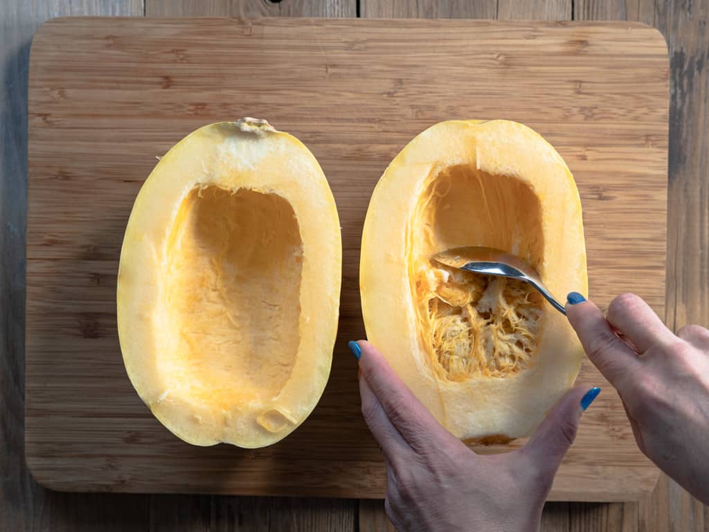 spaghetti squash cut in half with seeds being scraped out