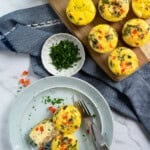 Baked egg bites on a wood board and on a serving plate. One is cut in half to show the ingredients inside.