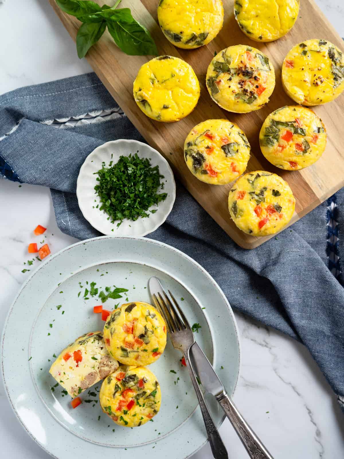 Baked egg bites on a wood board and on a serving plate. One is cut in half to show the ingredients inside.