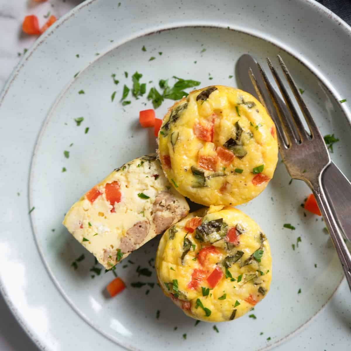 Two and a half egg bites on a plate. The half one is cut side up to show the ingredients inside.