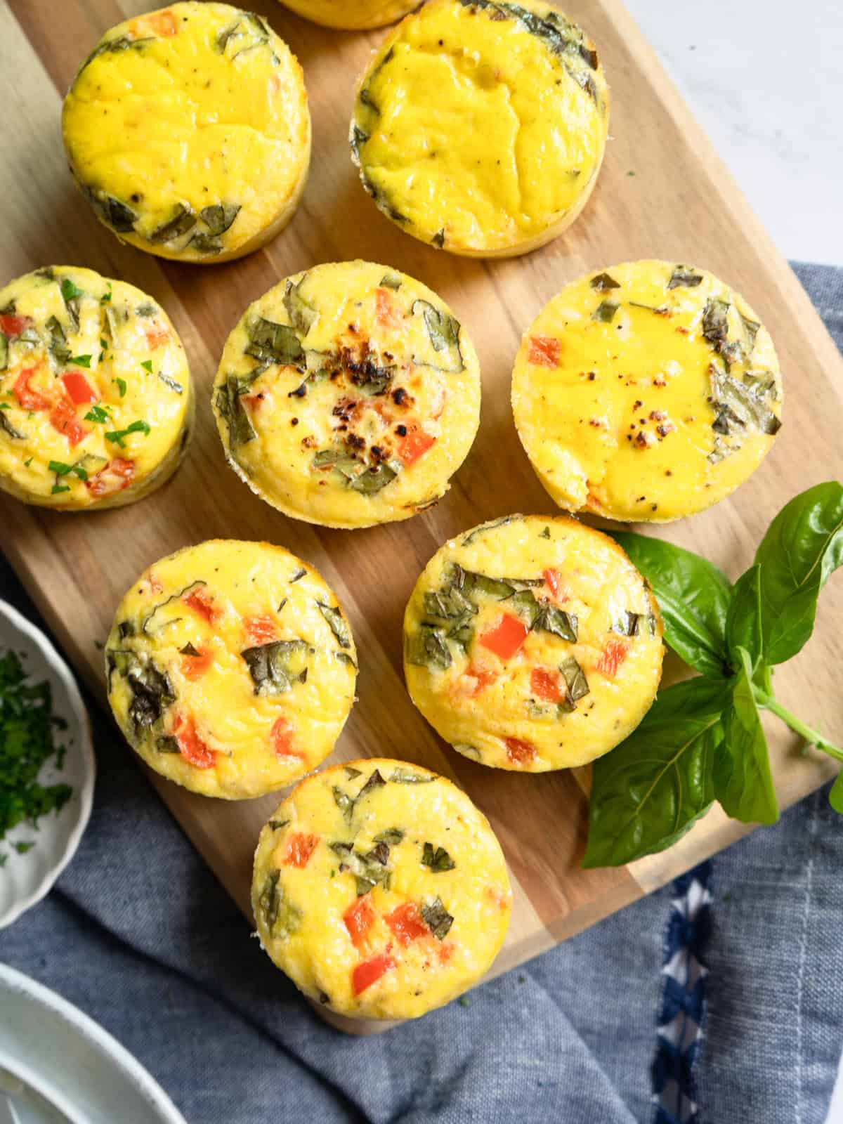 Baked egg bites on a wooden board garnished with fresh basil.