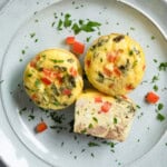 Two and a half egg bites on a plate. The half one is cut side up to show the ingredients inside.