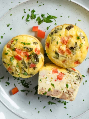 Two and a half egg bites on a plate. The half one is cut side up to show the ingredients inside.