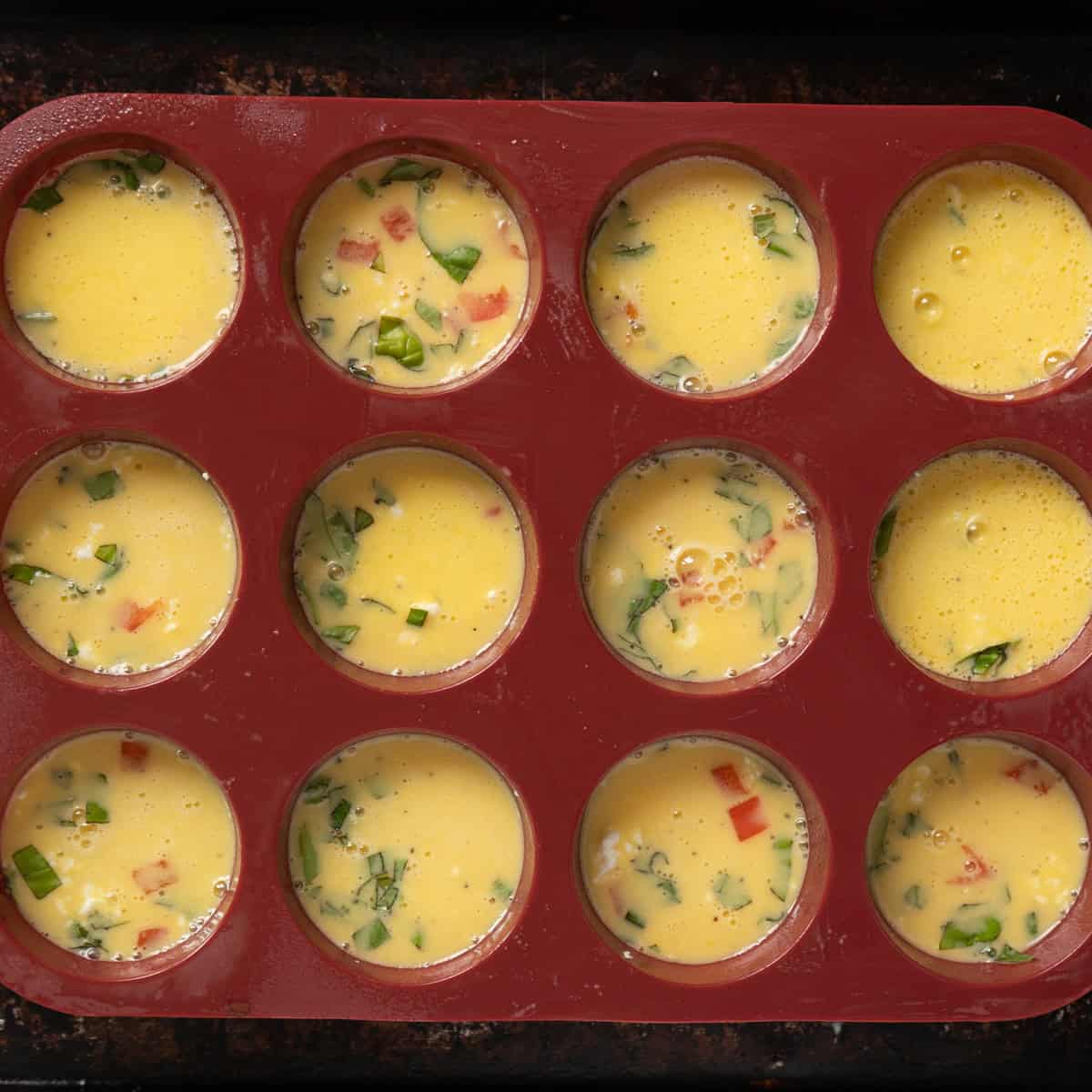 Egg mixture and fillings in a silicone pan to make egg bites.