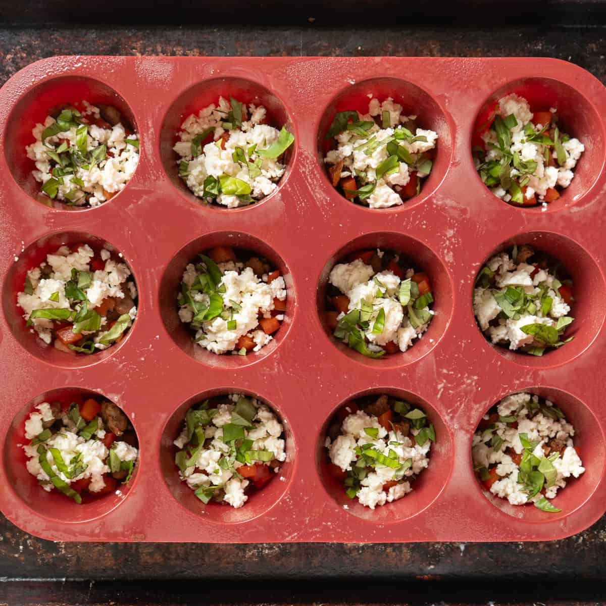 Filling ingredients in the cups of a 12-cup silicone muffin pan.