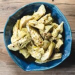 marinated artichoke hearts in a blue ceramic dish on a wooden background.