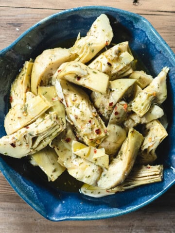 marinated artichoke hearts in a blue ceramic dish on a wooden background.