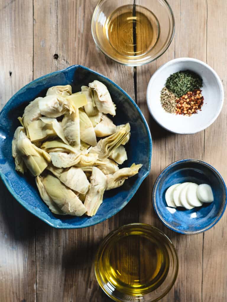 ingredients for making marinated artichoke hearts on a wooden board.