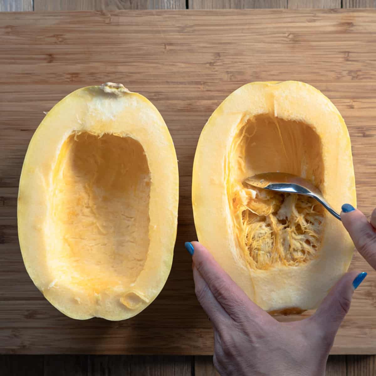 a spaghetti squash cut in half and seeds are being scraped out of the middle with a spoon. 