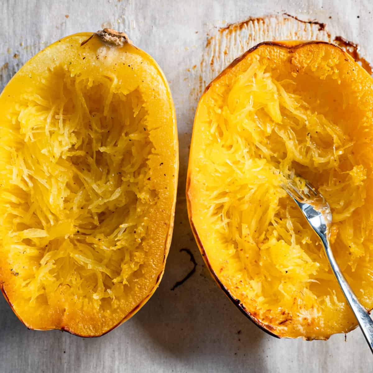 roasted squash halves with strands being loosened with a fork.