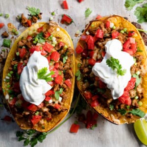 2 halves of stuffed spaghetti squash on a baking tray topped with sour cream.