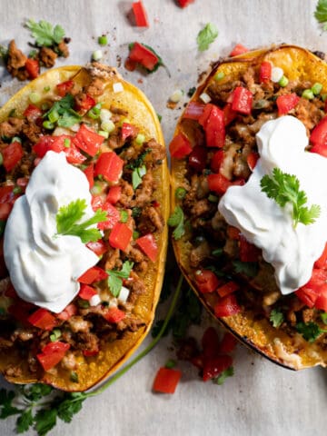 2 halves of stuffed spaghetti squash on a baking tray topped with sour cream.