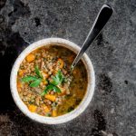 One bowl of lentil and bacon soup with a spoon on stone background