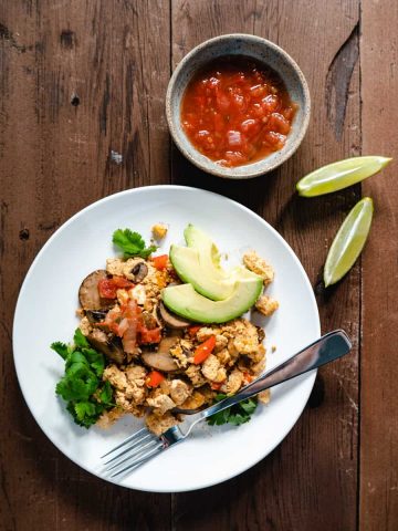 tofu scramble on white plate with avocado lime and salsa on the side