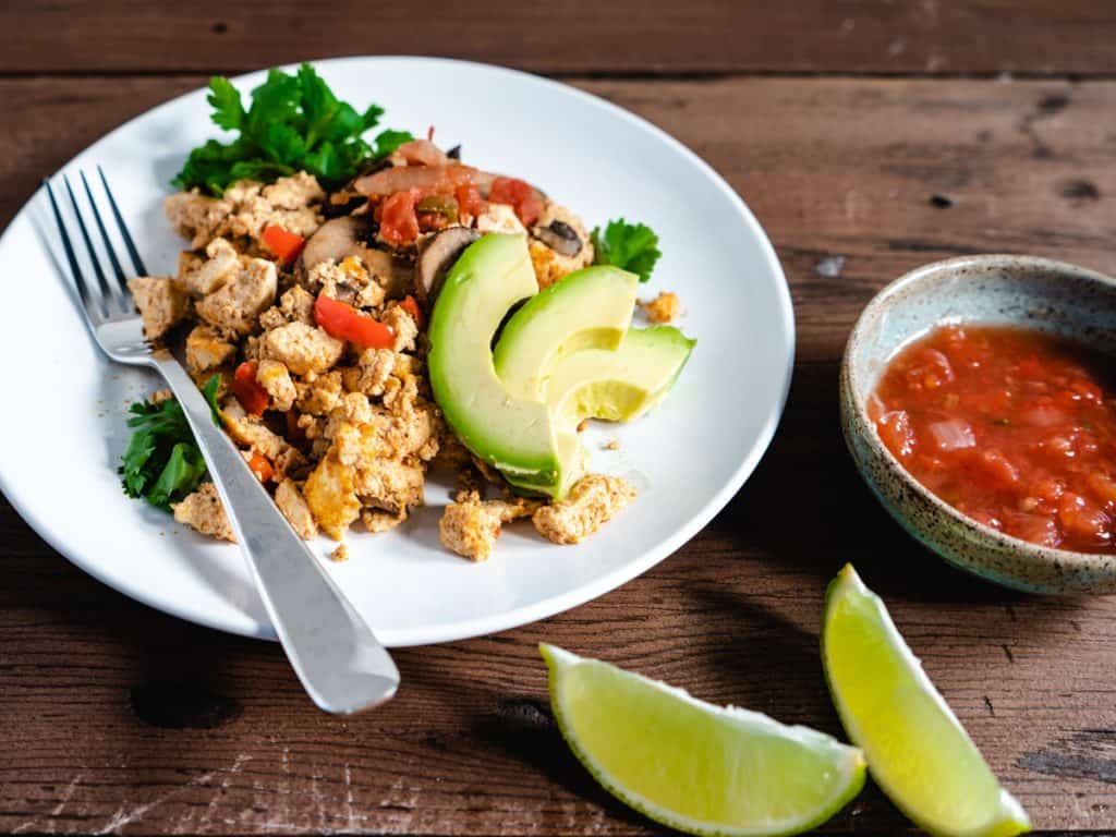 tofu scramble on white plate with avocado lime and salsa on the side