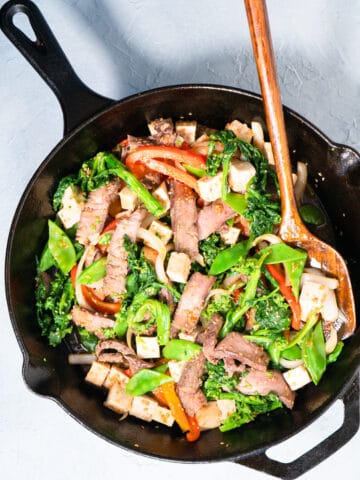 finished stir fry in a cast iron skillet with a wooden serving spoon.