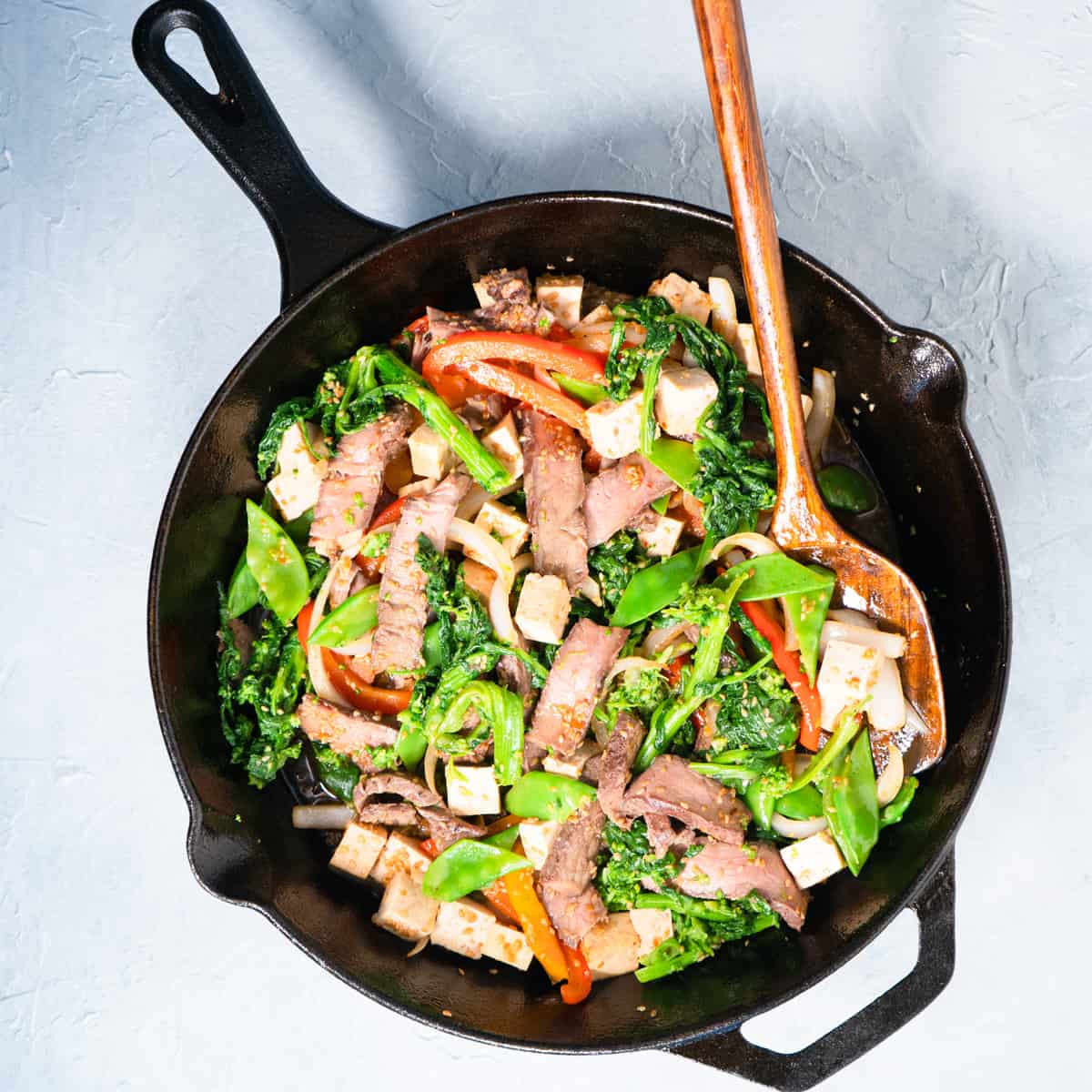 finished stir fry in a cast iron skillet with a wooden serving spoon. 