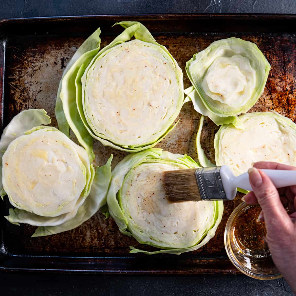 sliced cabbage on a baking sheet being brushed with bacon fat.
