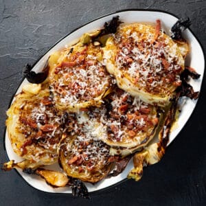 finished cabbage steaks on an oval serving platter topped with bacon and cheese.