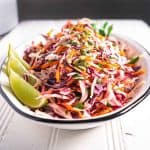 cumin lime coleslaw on white platter garnished with lime wedges
