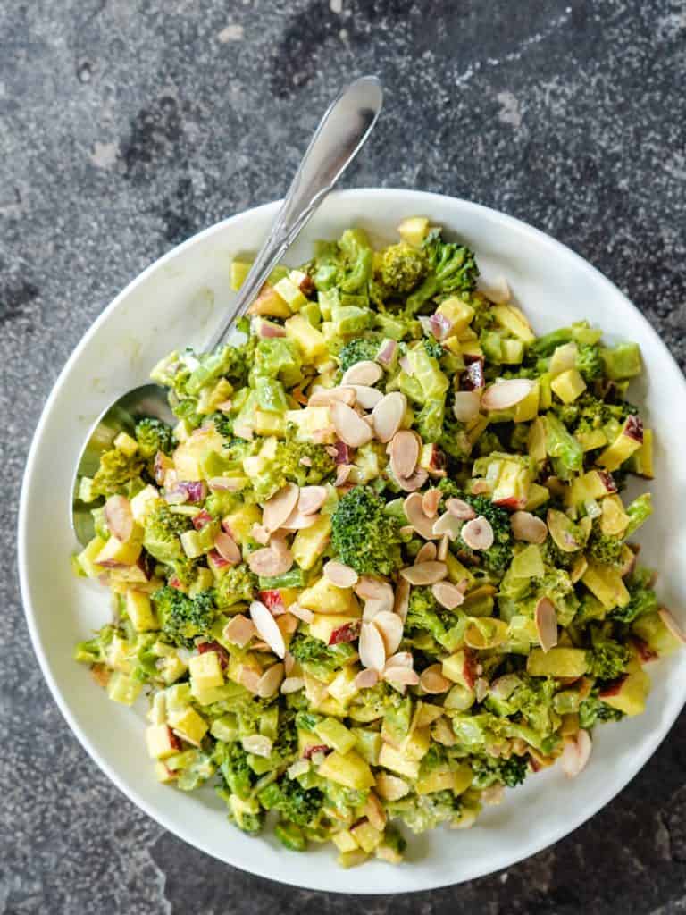 Broccoli salad on white plate with spoon on stone background