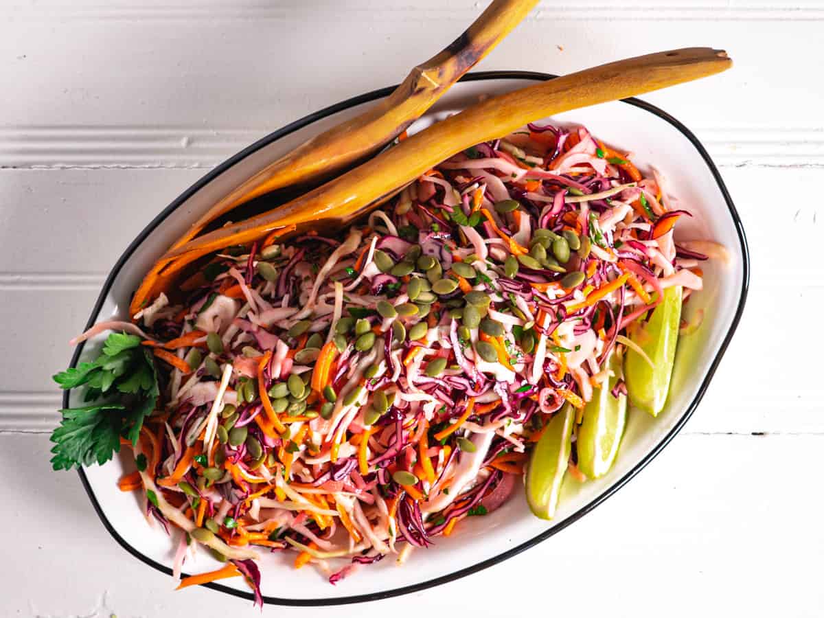 cumin lime coleslaw on white platter garnished with lime wedges