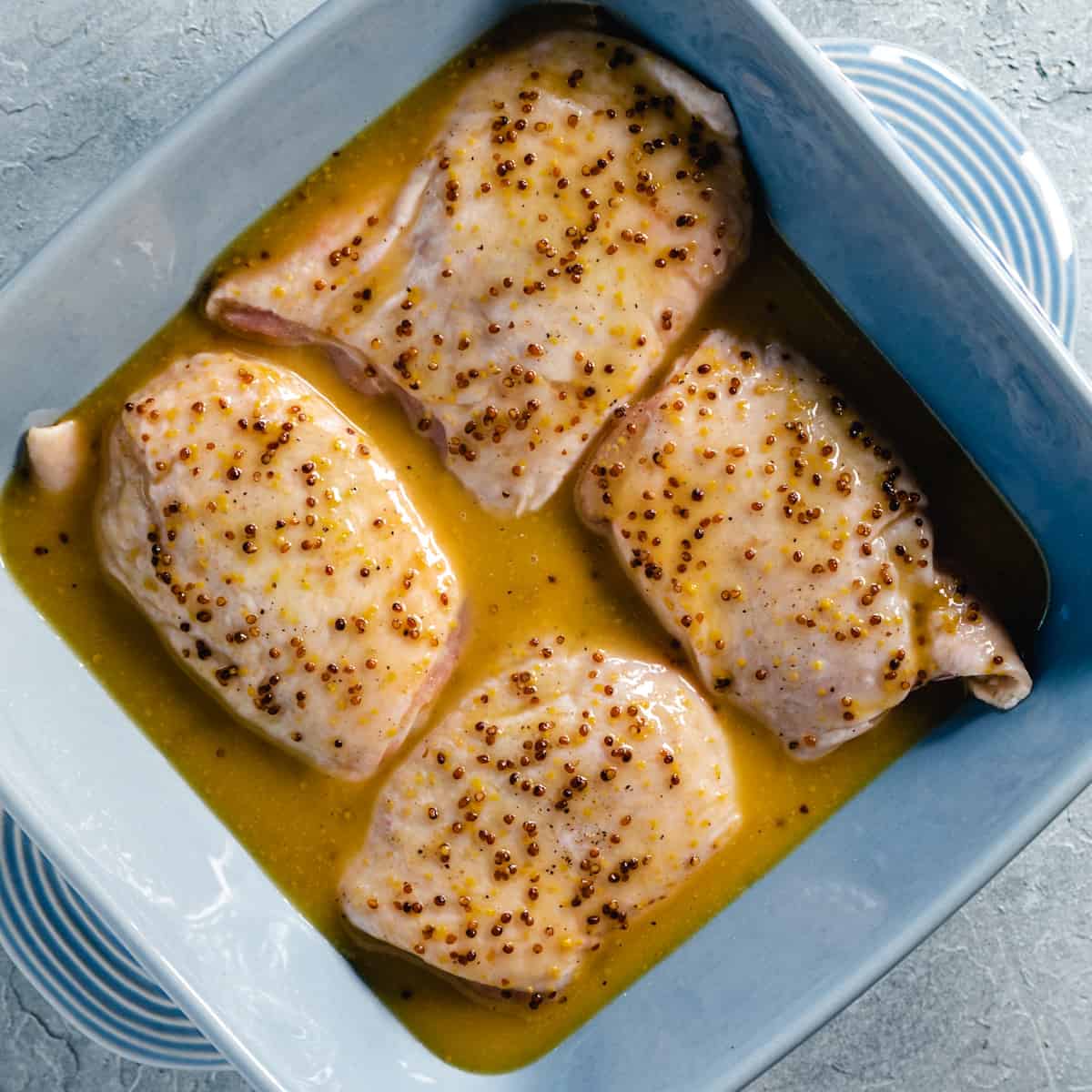 four chicken thighs in blue baking dish with honey mustard marinade