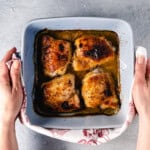 four baked chicken thighs in square blue dish being held with kitchen towel